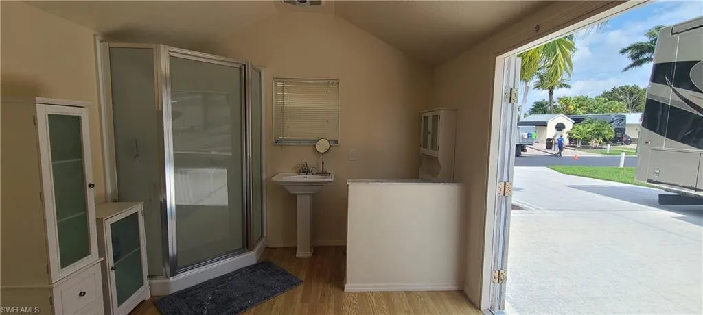 Bathroom featuring a sink, wood finished floors, baseboards, vaulted ceiling, and a stall shower