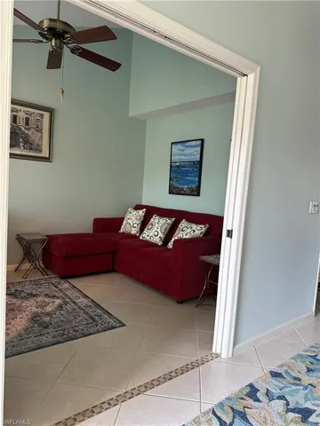 Living area with ceiling fan, light tile patterned flooring, and lofted ceiling
