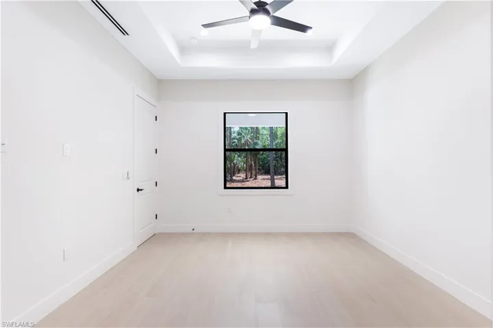 Primary bedroom with a raised ceiling, wood-like tile and ceiling fan
