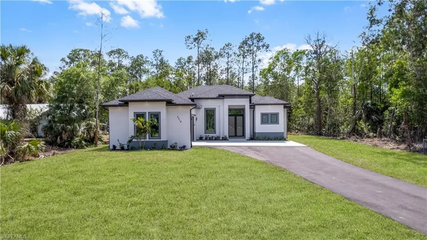 Prairie-style home with a front lawn, stucco siding, driveway, and view of wooded area