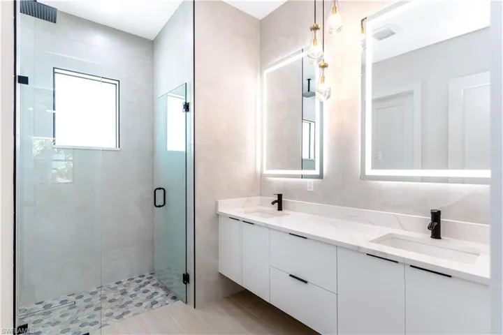 Primary bathroom with double vanity, a stall shower, and tile walls