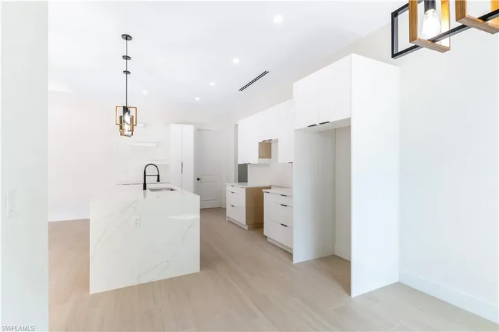 Kitchen with hanging light fixtures, wood-look tile, light stone countertops, and white cabinets