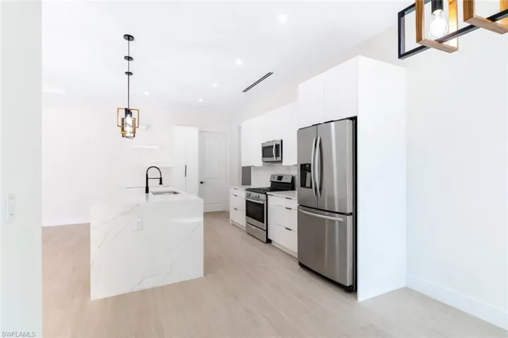 Kitchen featuring pendant lighting, stainless steel appliances, white cabinetry, and light stone counters