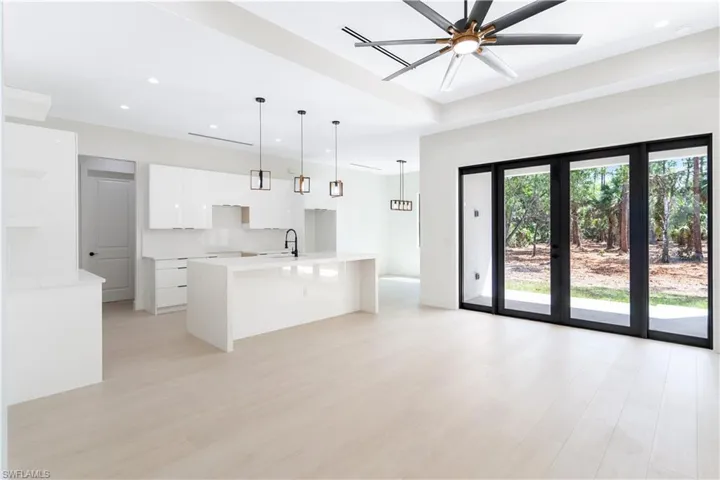 Kitchen with an island with sink, wood-look tile, light stone countertops, hanging light fixtures, and white cabinetry