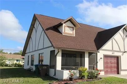 Tudor home featuring a front yard, stucco siding, roof with shingles, and concrete driveway