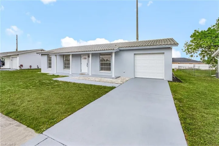 Ranch-style home featuring a tile roof, fence, an attached garage, and a front yard