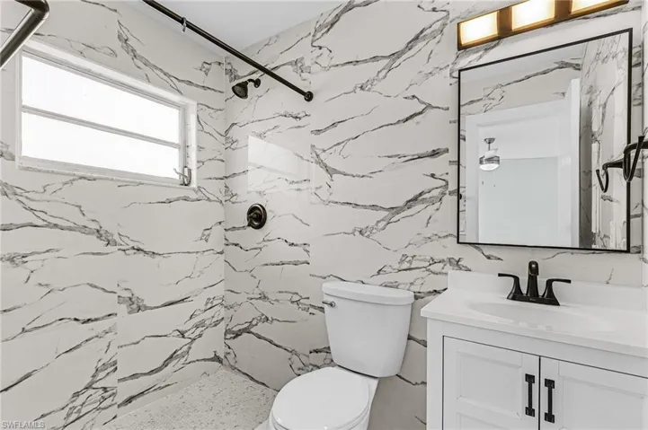 Bathroom with toilet, vanity, and a marble finish shower