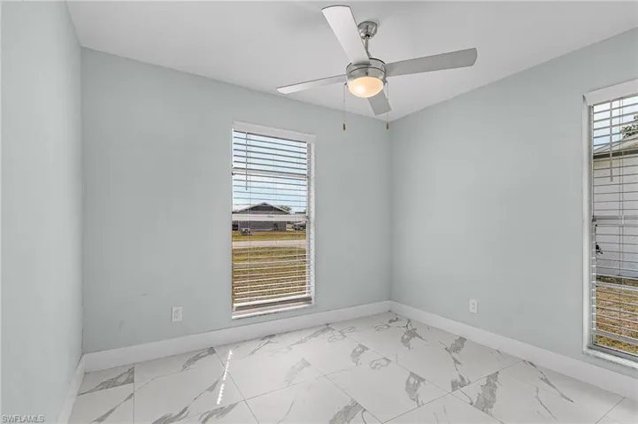 Empty room featuring baseboards, marble finish floor, and ceiling fan