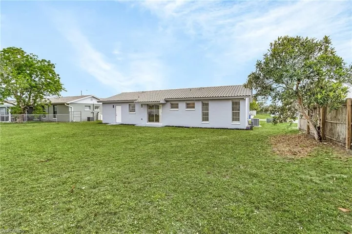 Rear view of house with fence, a lawn, a tiled roof, and stucco siding