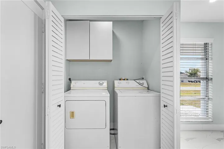 Clothes washing area with cabinet space, washing machine and dryer, and marble finish floor