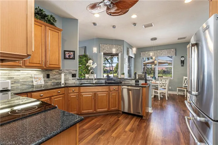 Kitchen with pendant lighting, appliances with stainless steel finishes, a sink, dark stone counters, and a peninsula