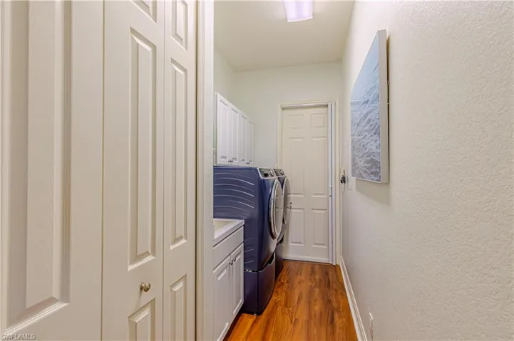 Clothes washing area with cabinet space, baseboards, washer and clothes dryer, a textured wall, and dark wood-style floors