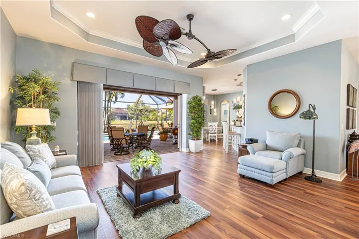 Living area featuring baseboards, a ceiling fan, dark wood-style flooring, a tray ceiling, and crown molding