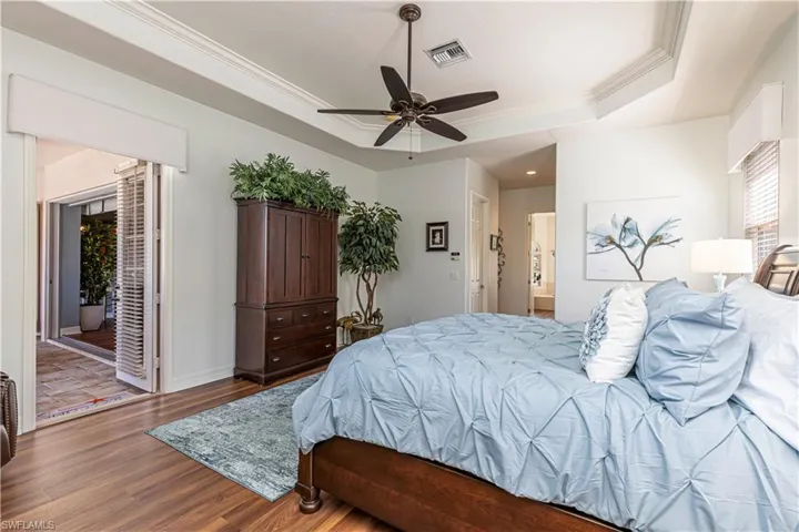 Bedroom featuring baseboards, visible vents, a raised ceiling, dark wood-type flooring, and crown molding
