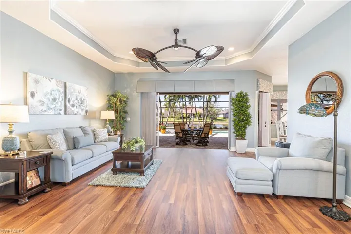Living room with ceiling fan, wood finished floors, a raised ceiling, and crown molding
