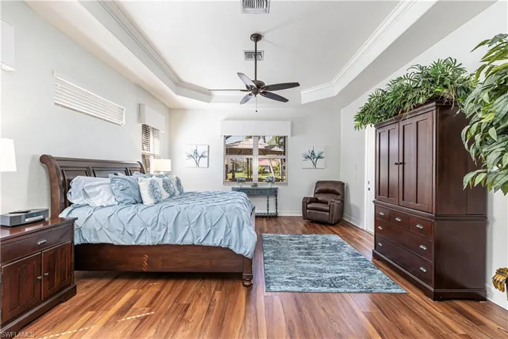 Bedroom featuring ornamental molding, a raised ceiling, dark wood-type flooring, and visible vents
