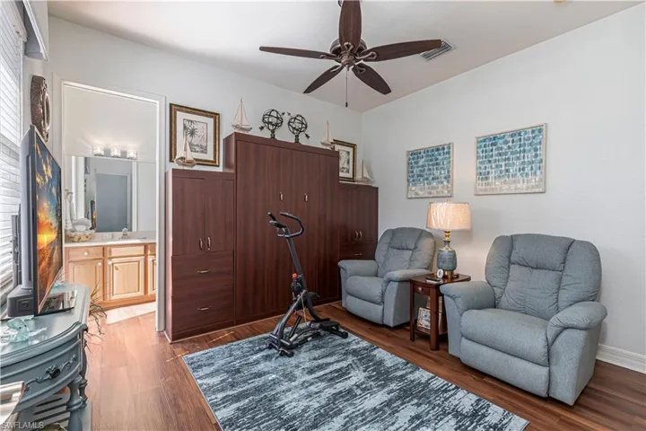 Living area with ceiling fan, dark wood finished floors, visible vents, and baseboards