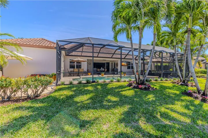 Rear view of property with a tile roof, stucco siding, a lawn, a patio area, and glass enclosure