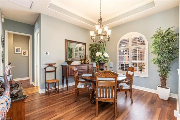 Dining space with dark wood-style floors, a raised ceiling, a chandelier, and baseboards