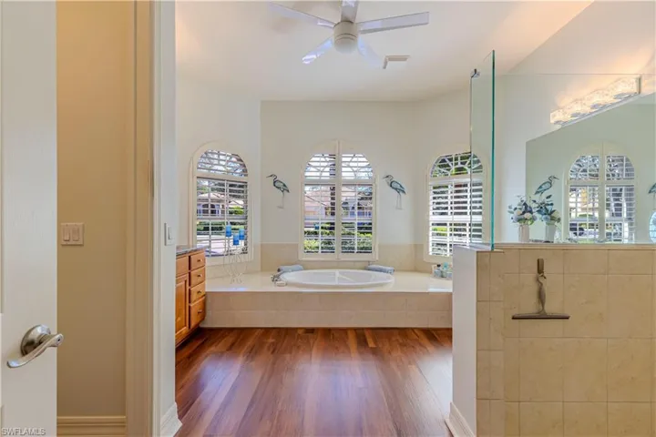 Bathroom with a ceiling fan, wood finished floors, vanity, a walk in shower, and a bath