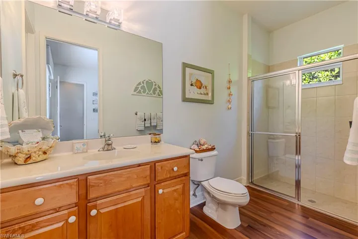 Full bath with toilet, a stall shower, vanity, wood finished floors, and baseboards