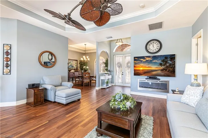 Living room with visible vents, a raised ceiling, dark wood-type flooring, and ceiling fan with notable chandelier