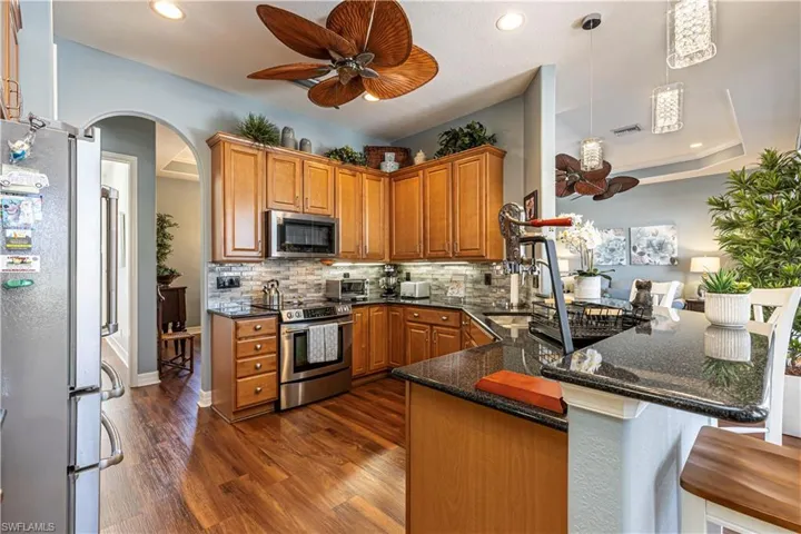 Kitchen featuring arched walkways, a peninsula, hanging light fixtures, appliances with stainless steel finishes, and dark stone counters