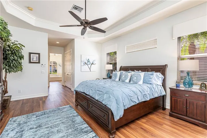 Bedroom featuring wood finished floors, a raised ceiling, visible vents, and baseboards
