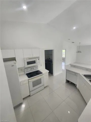 Kitchen with white cabinetry, lofted ceiling, white appliances, light tile patterned floors, and pendant lighting