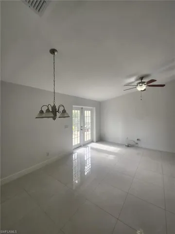 Spare room with ceiling fan with notable chandelier, french doors, and light tile patterned floors
