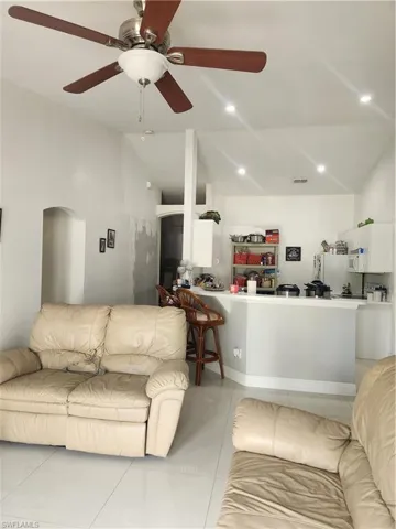 Living room with ceiling fan, light tile floors, and lofted ceiling