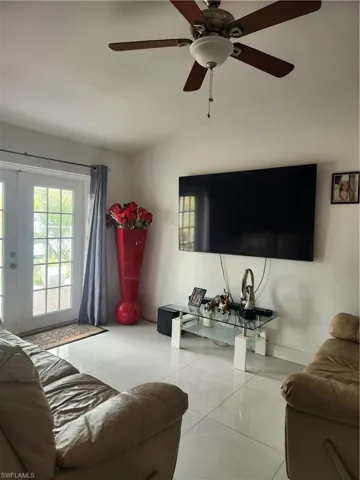 Tiled living room featuring ceiling fan, vaulted ceiling, and french doors