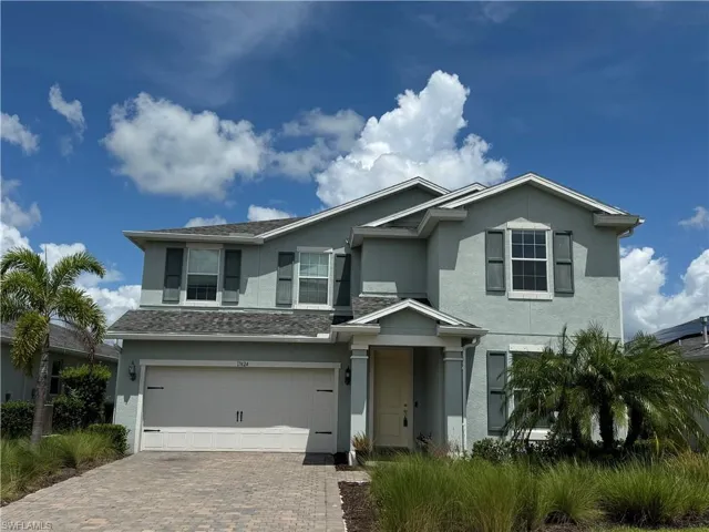 Two-story stucco residence featuring a two-car garage, covered entry, and a paver driveway