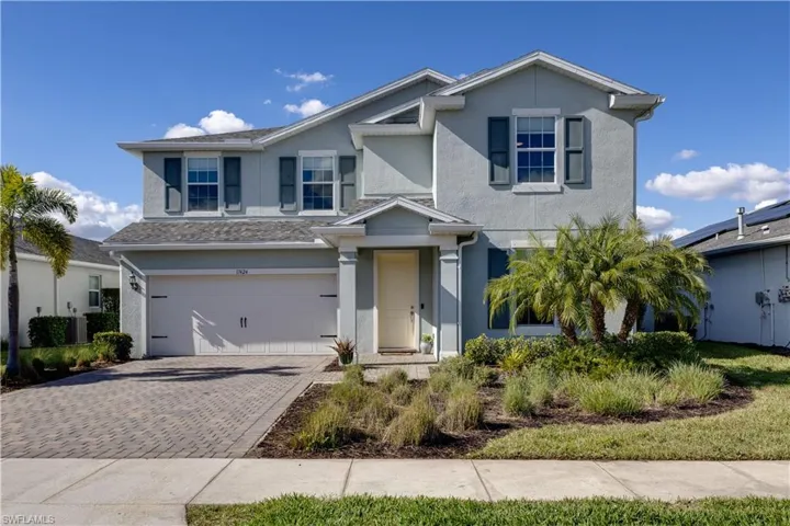 Two-story stucco exterior featuring a two-car garage, paver driveway, and mature landscaping