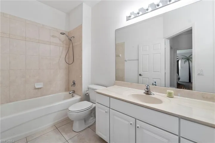 Bathroom featuring a full-sized bathtub with tiled surround, a white toilet, and a vanity with a light-toned countertop and integrated sink