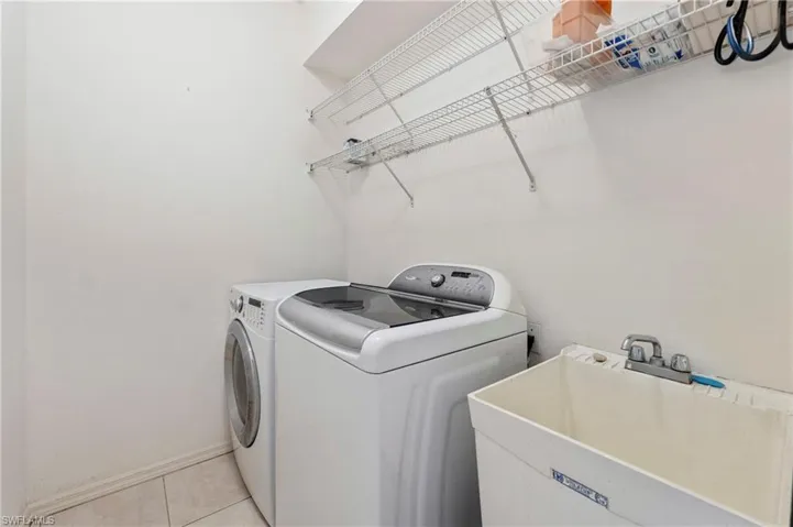 Dedicated laundry space featuring a utility sink, wall-mounted wire shelving, and tile flooring