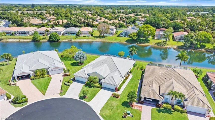 Waterfront property featuring a tile roof, mature palm trees, manicured lawns, and a paved driveway leading to an attached garage