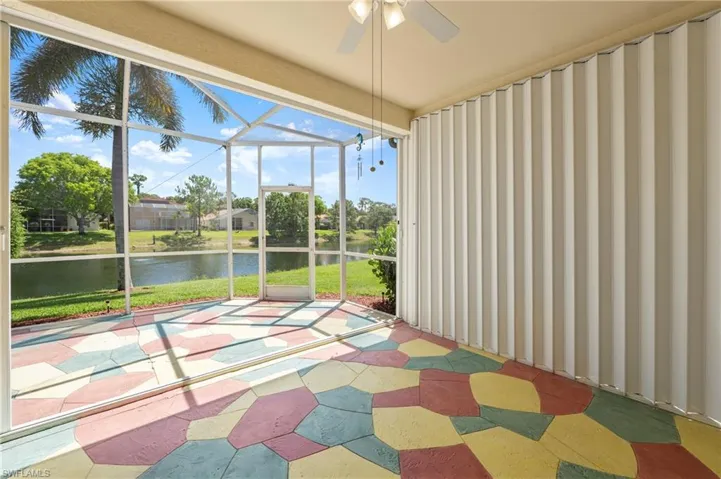 Screened lanai featuring a colorful geometric-patterned floor, ceiling fan, and accordion hurricane shutters
