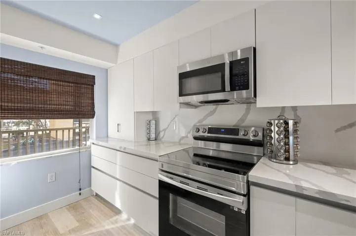 Kitchen featuring light stone counters, modern cabinets, stainless steel appliances, light wood-style flooring, and white cabinets