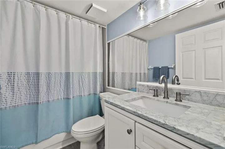 Bathroom with toilet, vanity, visible vents, and shower / bathtub combination with curtain