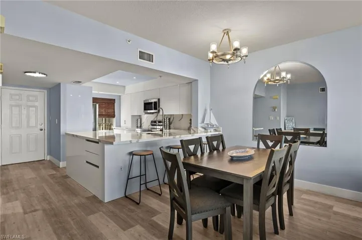 Dining room with light wood-type flooring, arched walkways, baseboards, a notable chandelier, and visible vents