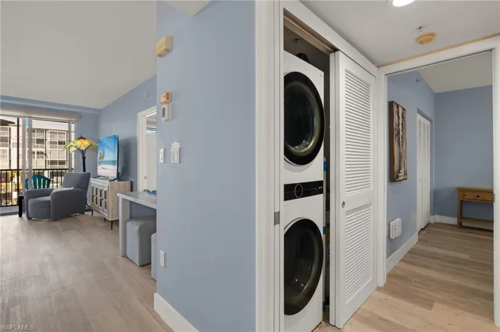 Laundry area featuring baseboards, stacked washing maching and dryer, laundry area, and light wood-type flooring