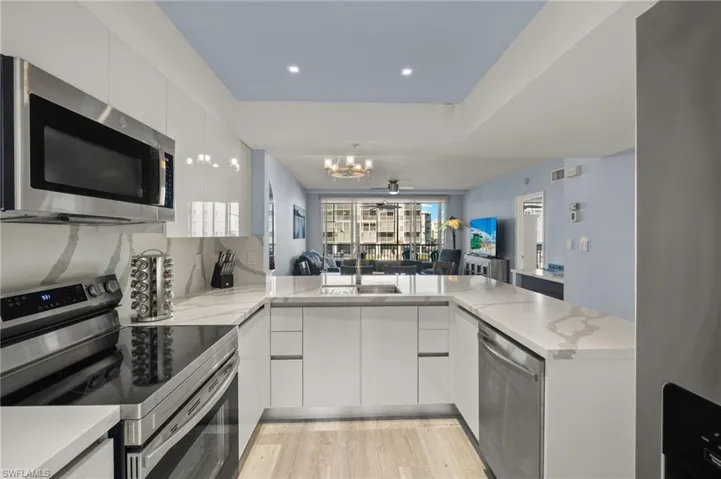 Kitchen with white cabinets, an inviting chandelier, stainless steel appliances, and modern cabinets