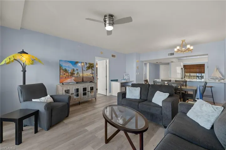Living area with visible vents, light wood finished floors, and ceiling fan with notable chandelier