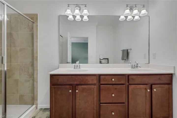 Bathroom featuring a shower stall, double vanity, crown molding, and suspended lighting