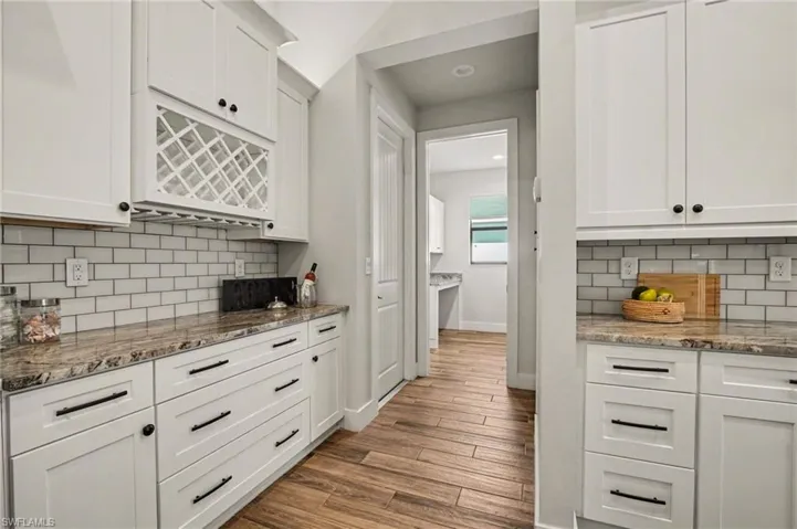 Kitchen with white cabinetry, light stone counters, light wood-type flooring, and backsplash