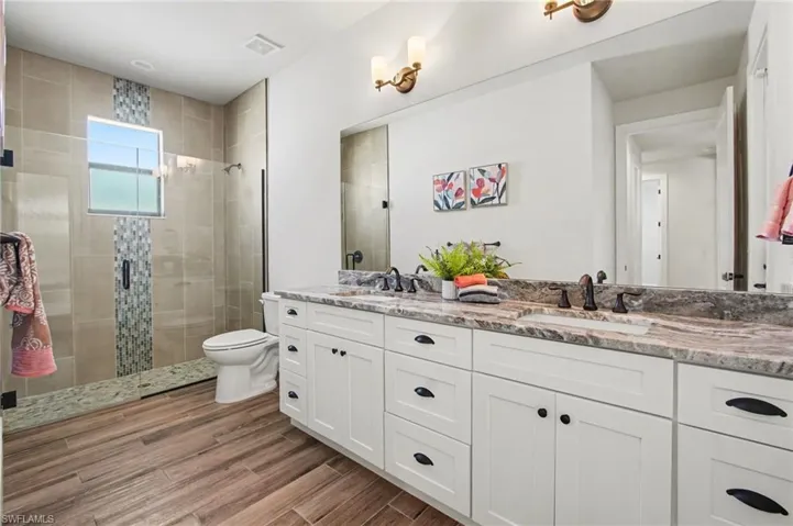 Bathroom featuring double vanity, a stall shower, and light wood-style floors