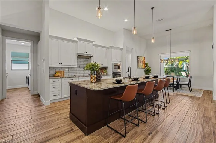 Dual tone kitchen featuring two tone cabinets, a kitchen breakfast bar, a center island with sink, decorative light fixtures, and light stone countertops