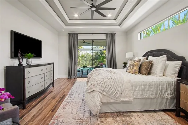 Bedroom featuring wood finished floors, ceiling fan, access to exterior, ornamental molding, and a tray ceiling