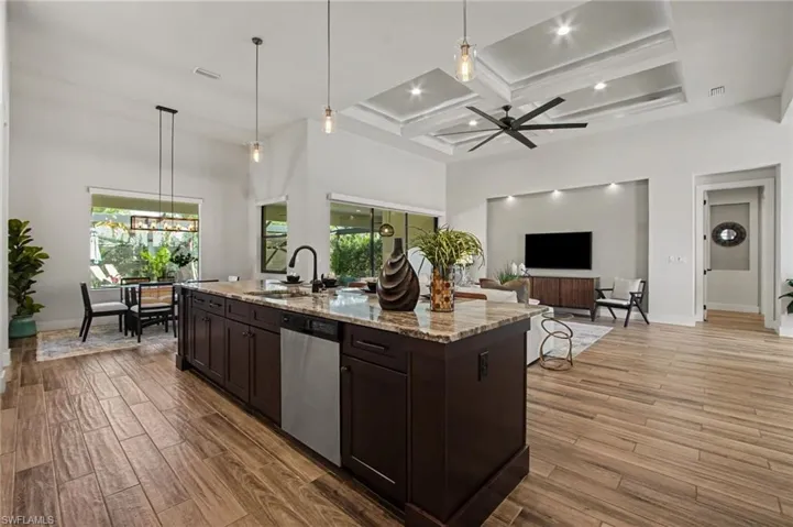 Kitchen with hanging light fixtures, dark wood finish cabinetry, light stone counters, light wood finished floors, and coffered ceiling